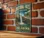 A vintage-style metal sign for Natural Falls State Park in Oklahoma, featuring a waterfall and lush greenery.