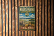 A vintage-style metal sign for theNGORONGORO CONSERVATION AREA in Tanzania, featuring an illustration of a rhinoceros and a lion in a grassy landscape.