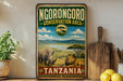 A vintage-style sign for theNGORONGORO Conservation Area in Tanzania, featuring an illustration of a rhinoceros and a lion in a grassy savanna landscape.