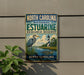 A metal sign for the North Carolina Estuarine Research Reserve, featuring a lighthouse and a bird in a grassy area.