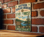 A vintage-style metal sign for the Northern Highland-American State Forest in Wisconsin, featuring a scenic illustration of a forest landscape with a river and pine trees.