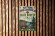 A vintage metal sign for the Northern Highland-American State Forest in Wisconsin, featuring a scenic landscape with pine trees, a river, and a sign indicating the location.