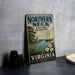 A vintage metal sign for the Northern Neck National Heritage Area in Virginia, featuring a sailboat and a lighthouse, is displayed on a gray countertop next to some black camera lenses.