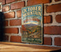 A vintage metal sign for October Mountain State Forest in Massachusetts, featuring a scenic mountain landscape and inviting visitors to explore the area.