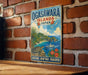 A vintage-style metal sign with a tropical island landscape and a boat, mounted on a brick wall.