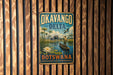 A vintage-style metal sign with the text "OKAVANGO DELTA BOTSWANA" and an illustration of a man in a boat on a river surrounded by wildlife.