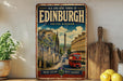 a vintage-style metal sign with a picture of a city street and a red double-decker bus, along with the text "Old and New Towns of Edinburgh United Kingdom" and "Where history meets harmony".