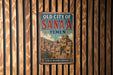 a vintage-style metal sign with the text "OLD CITY OF SANA'A YEMEN" and "LAND OF HISTORY & HERITAGE" on it, mounted on a wooden wall.