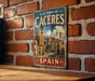 A vintage metal sign with the text "OLD TOWN OF CÁCERES" and "SPAIN" is displayed on a brick wall.