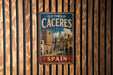 A vintage metal sign that reads "Old Town of Cáceres, Spain" is displayed on a wooden wall.
