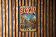 A vintage metal sign with the text "Old Town of Segovia & its Aqueduct" and "SPAIN" is displayed on a wooden wall.