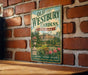 A vintage-style metal sign for Old Westbury Gardens in New York, featuring a garden scene with a large house and flowers.