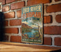 A vintage-style metal sign with the text "ORD RIVER FLOODPLAIN AUSTRALIA" and a scenic illustration of a river surrounded by mountains and vegetation.
