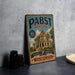 A vintage-style metal sign for Pabst mansion, featuring an illustration of a grand mansion with a tree in the foreground.
