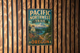 A metal sign with the text "PACIFIC NORTHWEST TRAIL OREGON" is displayed on a wooden wall.