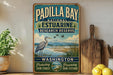 A vintage-style sign for Padilla Bay National Estuarine Research Reserve, featuring a bird, a lake, and mountains in the background.
