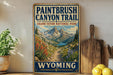 A vintage-style sign for the Paintbrush Canyon Trail in Grand Teton National Park, with a scenic mountain landscape and a path leading through the valley.