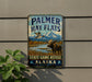 A vintage metal sign for Palmer Hay Flats, featuring a moose and a bird in a scenic landscape, with mountains in the background.