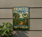 A metal sign on a wall, featuring a palm tree and a trail, with the text "Palmetto Trail" and "South Carolina Hiking, Nature, Adventure" displayed.