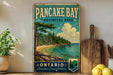 A vintage-style sign for Pancake Bay Provincial Park in Ontario, Canada, featuring a scenic landscape with pine trees, a beach, and a lake.