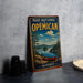 A vintage-style metal sign for the PARC NATIONAL D'OPEMICAN, featuring a scenic landscape with a lake, mountains, and a canoe, is displayed on a gray countertop.