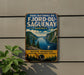 A vintage-style metal sign with a scenic image of a mountain landscape and a river, advertising the park of Fjord-du-Saguenay, Quebec.