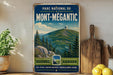 A vintage-style metal sign for the park of Mont-Megantic, featuring a mountain landscape with pine trees and a dome structure.