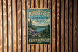 A vintage metal sign for Paugusset State Forest in Connecticut, featuring a scenic landscape with pine trees, a lake, and mountains.
