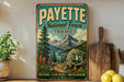 A vintage-style metal sign for the Payette National Forest in Idaho, featuring a scenic mountain landscape with pine trees, a lake, and a path leading through the forest.