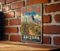 A vintage-style metal sign with a desert landscape and cacti, mounted on a brick wall.