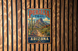 A vintage metal sign for the Peralta Trail in Arizona, featuring a desert landscape with mountains, cacti, and a dirt path.