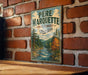 A vintage metal sign with the text "PERE MARQUETTE STATE FOREST MICHIGAN" is displayed on a brick wall.