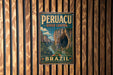 A vintage-style metal sign with the text "PERUACU RIVER CANYON BRAZIL" and a scenic illustration of a river canyon, mounted on a wooden wall.