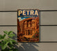 A vintage-style metal sign with the text "PETRA JORDAN" and an illustration of the ancient city of Petra, featuring a camel and a temple.
