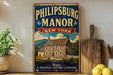 A vintage-style metal sign for the historic Philipburg Manor in New York, featuring an illustration of a historic house surrounded by a wooden fence and mountains in the background.
