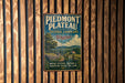 A vintage-style metal sign for Piedmont Plateau, Virginia, featuring a scenic landscape with a road, trees, and a house.