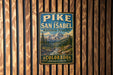 A vintage-style metal sign with the text "Pike and San Isabel National Forests" and "Colorado Adventure Awaits" is displayed on a wooden wall.