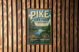 A vintage-style metal sign for Pike State Forest, Indiana, featuring a scenic image of the forest and a river.