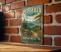 A vintage metal sign for the Pittsfield State Forest in Massachusetts, featuring a scenic landscape with pine trees, a lake, and mountains.
