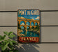 A vintage-style metal sign displaying the name "PONT DU GARD" and the location "AQUEDUC ROMAIN" is mounted on a wall, with a plant to the left.