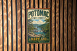 A vintage metal sign for Potomac State Forest in Maryland, featuring a scenic landscape with a river, mountains, and trees.
