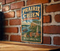 A vintage-style metal sign with the text "Prairie du Chien" and "Heritage Landscape" hangs on a brick wall.