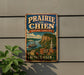 A vintage-style metal sign for Prairie du Chien, Wisconsin, featuring a scenic landscape with a river, buildings, and a church steeple.
