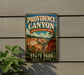 A vintage-style metal sign for Providence Canyon, Georgia's Little Grand Canyon State Park, mounted on a wall next to a plant.