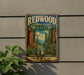 A vintage-style metal sign for Redwood National and State Parks, featuring a scenic illustration of a forest with towering redwood trees and a winding path.