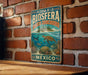A vintage-style metal sign with the text "RESERVA DE LA BIOSFERA BANCO CHINCHORRO" and "MEXICO" is displayed on a brick wall.