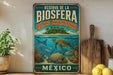 A vintage-style metal sign with the text "RESERVA DE LA BIOSFERA BANCO CHINCHORRO MEXICO" and an illustration of a tropical island with a sea turtle swimming among colorful coral and fish.