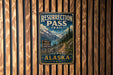 A vintage metal sign for the Resurrection Pass Trail in Alaska, featuring a scenic mountain landscape with a trail leading through it.