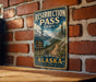 A vintage metal sign for the Resurrection Pass Trail in Alaska, featuring a scenic mountain landscape and trail marker.
