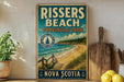 A vintage-style metal sign for Rissers Beach Provincial Park in Nova Scotia, featuring a scenic beach landscape with a wooden walkway leading to the shore.